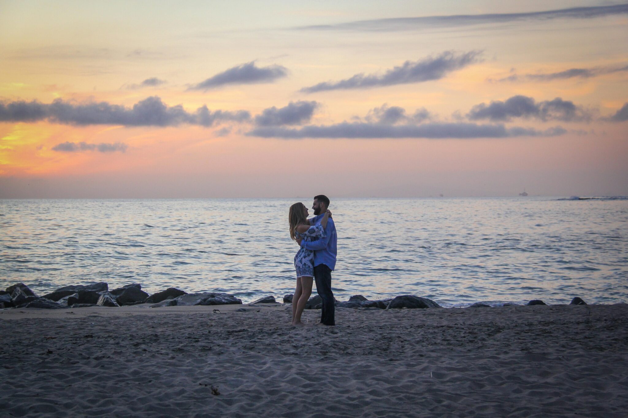 A man and woman standing on the beach at sunset.