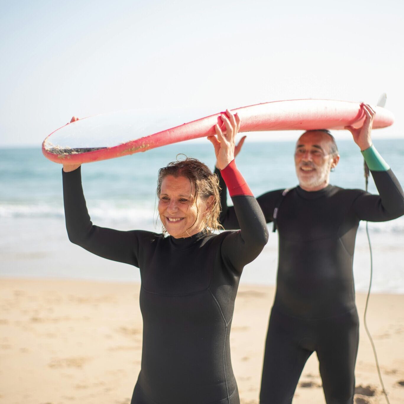 A man and woman holding up a surfboard on the beach.